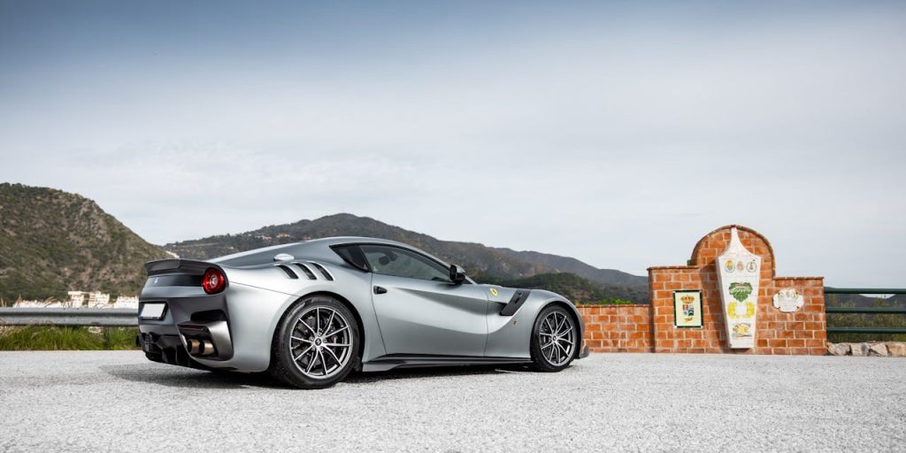 A silver sports car parked on a mountainous road with a scenic backdrop.